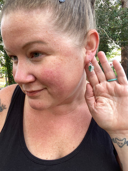 girl showing off pair of monstera earrings