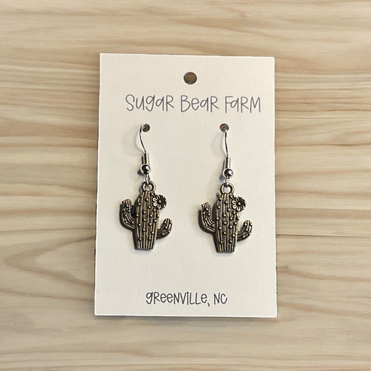 silver colored cactus earrings on wood