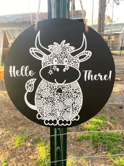 black door sign with a white cow and reads "hello there"