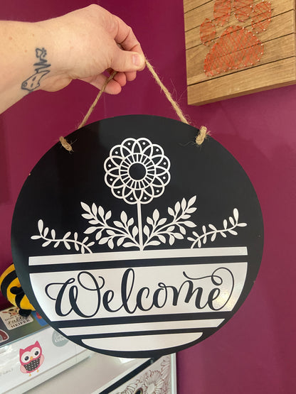 Black circle wooden door sign with flowers and reads "welcome"